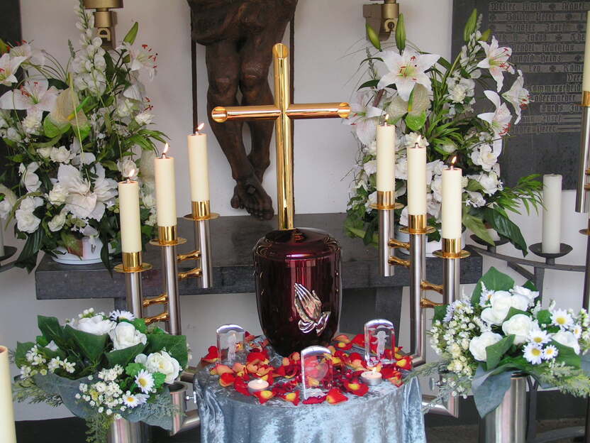 Altar mit goldenem Kreuz, dekoriert mit Blumen, Kerzen und einer Urne, umgeben von Rosenbl&auml;ttern.