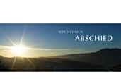 Sonnenaufgang &uuml;ber bergiger Landschaft mit dem Schriftzug &bdquo;Wir nehmen Abschied&ldquo; im Vordergrund.