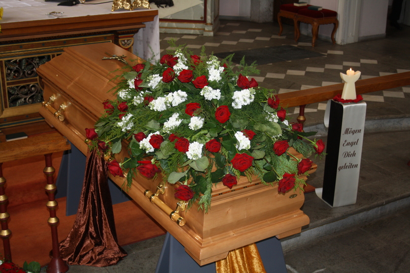 Holzkasten mit roten und wei&szlig;en Blumen sowie Gr&uuml;npflanzen, auf einem Tisch in einer Kirche.