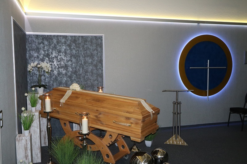 Holzschatulle steht in einem Raum mit Kerzen, Pflanzen und einem dekorativen Hintergrund. Brahmenbeleuchtung erg&auml;nzt die Stimmung.