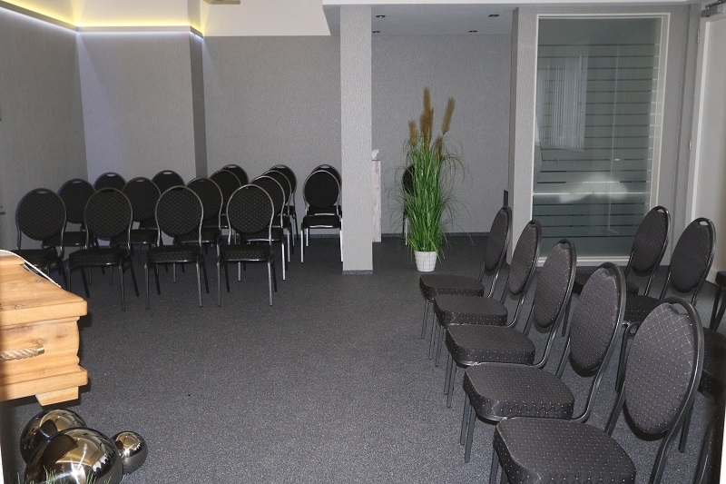 Raum mit mehreren schwarzen St&uuml;hlen, einer Pflanze und einem Tisch im Vordergrund, beleuchtet mit sanften Lichtakzenten.