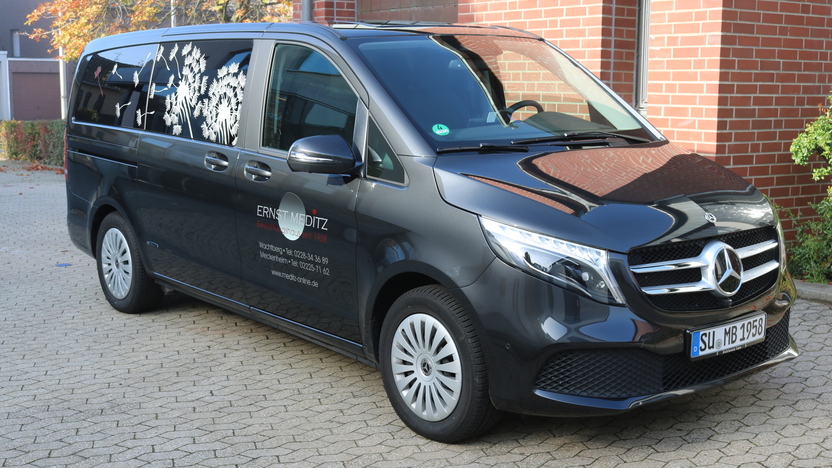 Schwarzer Mercedes-Van mit auff&auml;lliger Beschriftung, geparkt auf einer gepflasterten Einfahrt.