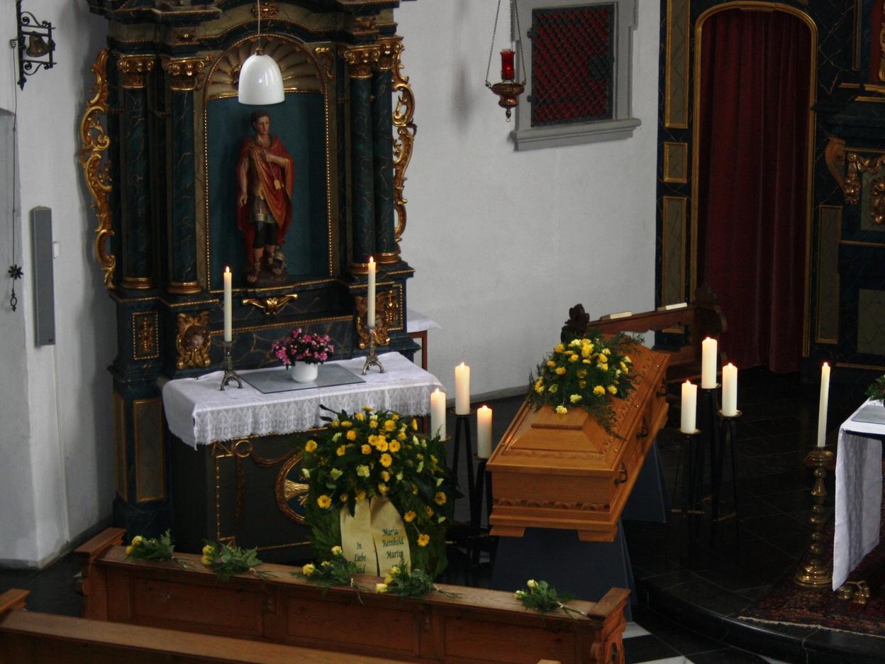 Innenansicht einer Kirche mit einem geschmückten Sarg, Kerzen, einem Altar und einem dekorierten Tisch.