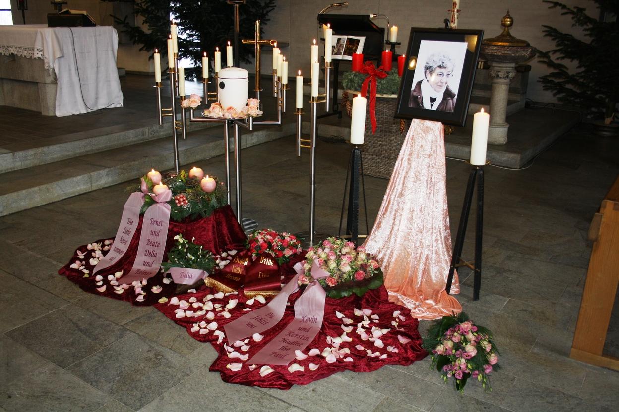 Gedenkst&auml;tte mit Kerzen, Blumen, einer Fotografie und Texttafeln auf einem Tisch in einem Kirchenraum.