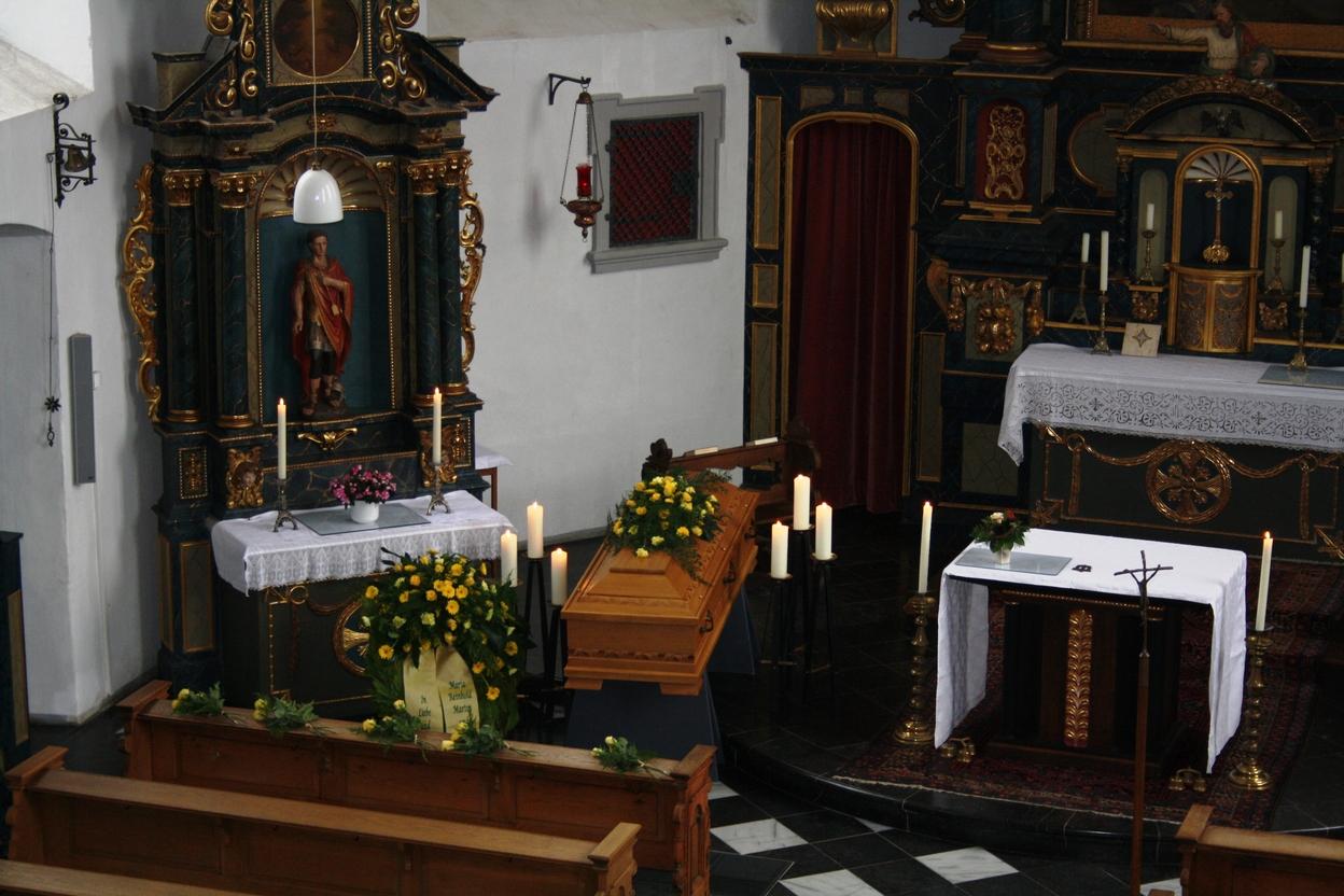 Innenansicht einer Kirche mit einem geschm&uuml;ckten Sarg, Kerzen, einem Altar und einem dekorierten Tisch.