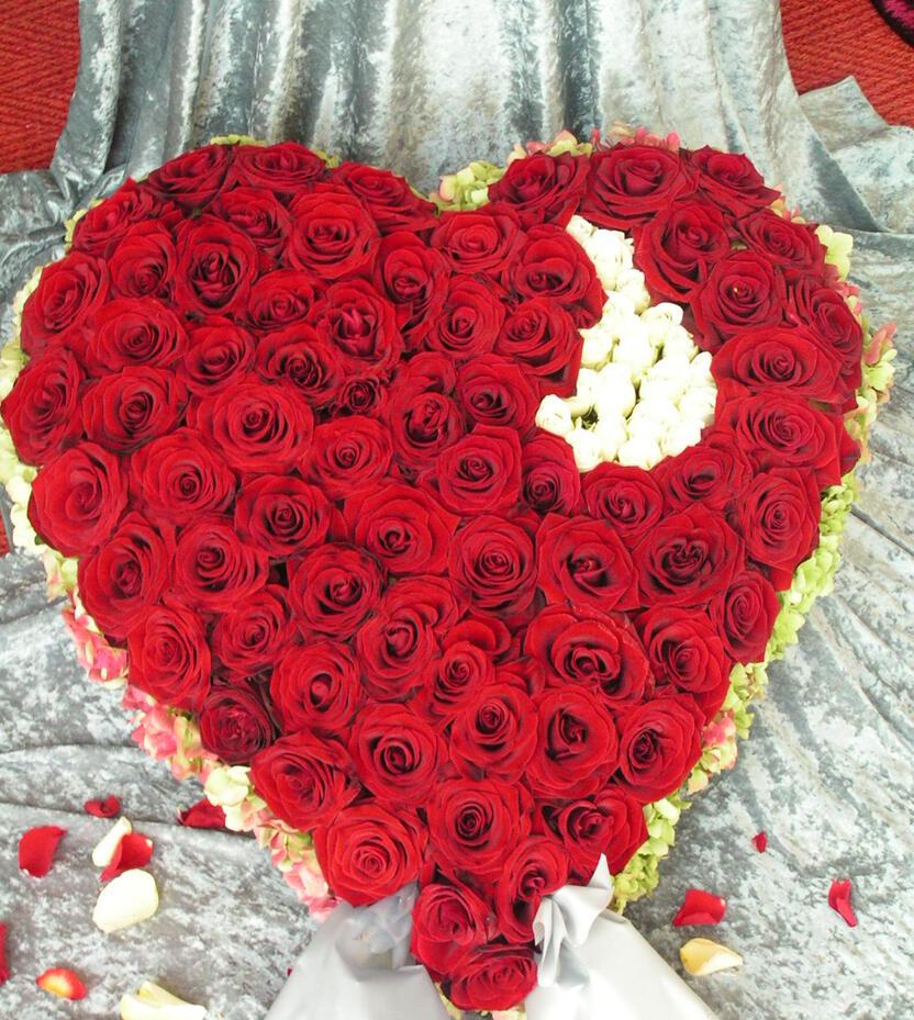 Herzf&ouml;rmiger Blumenstrau&szlig; aus roten Rosen, erg&auml;nzt mit wei&szlig;en Bl&uuml;ten, auf grauem Untergrund.