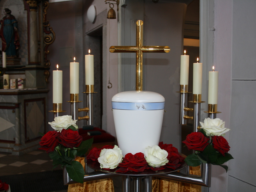 Gedeckter Altar mit einer Urne, goldener Kreuz, Kerzen und roten sowie wei&szlig;en Rosen.
