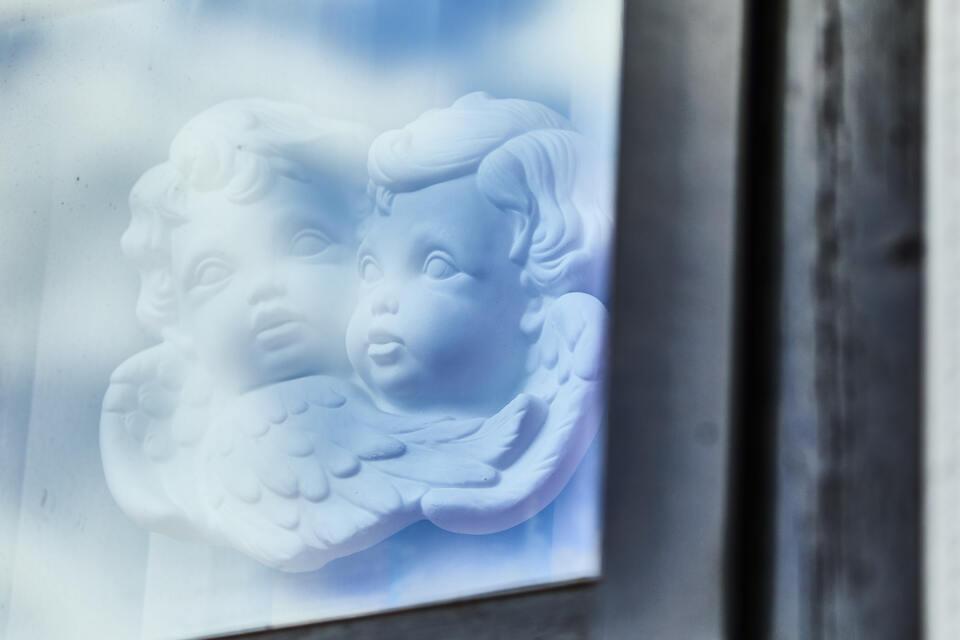 Relief von zwei puttoähnlichen Engelchen auf einer gläsernen Fläche mit reflektierendem Hintergrund.