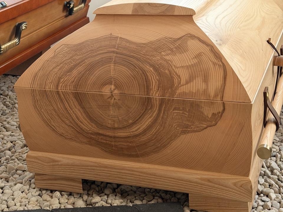 Holzurne mit nat&uuml;rlicher Maserung und Blumenarrangement auf der oberen Fl&auml;che, umgeben von zwei weiteren Urnen.