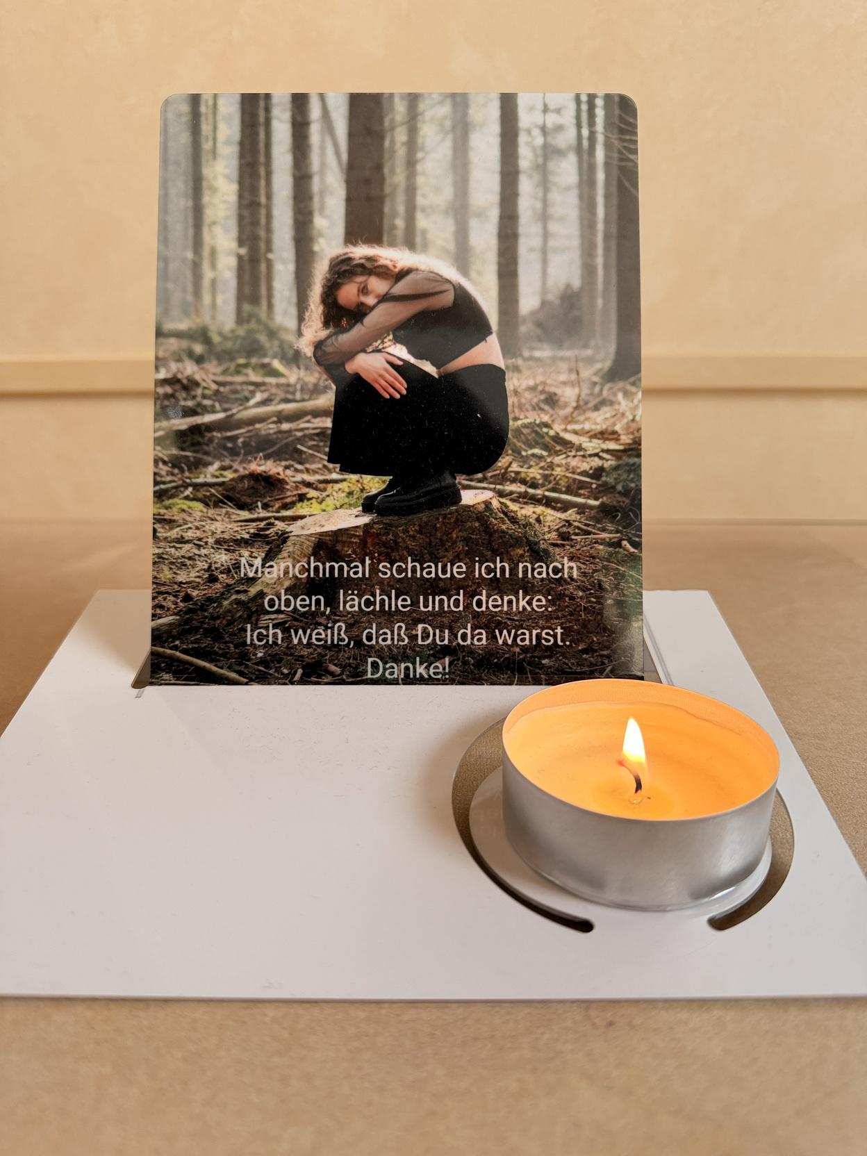 Karte mit einer Frau in einem Wald, die im Z Sitzen auf einem Holzfu&szlig;boden posiert, daneben eine brennende Teelichtkerze.