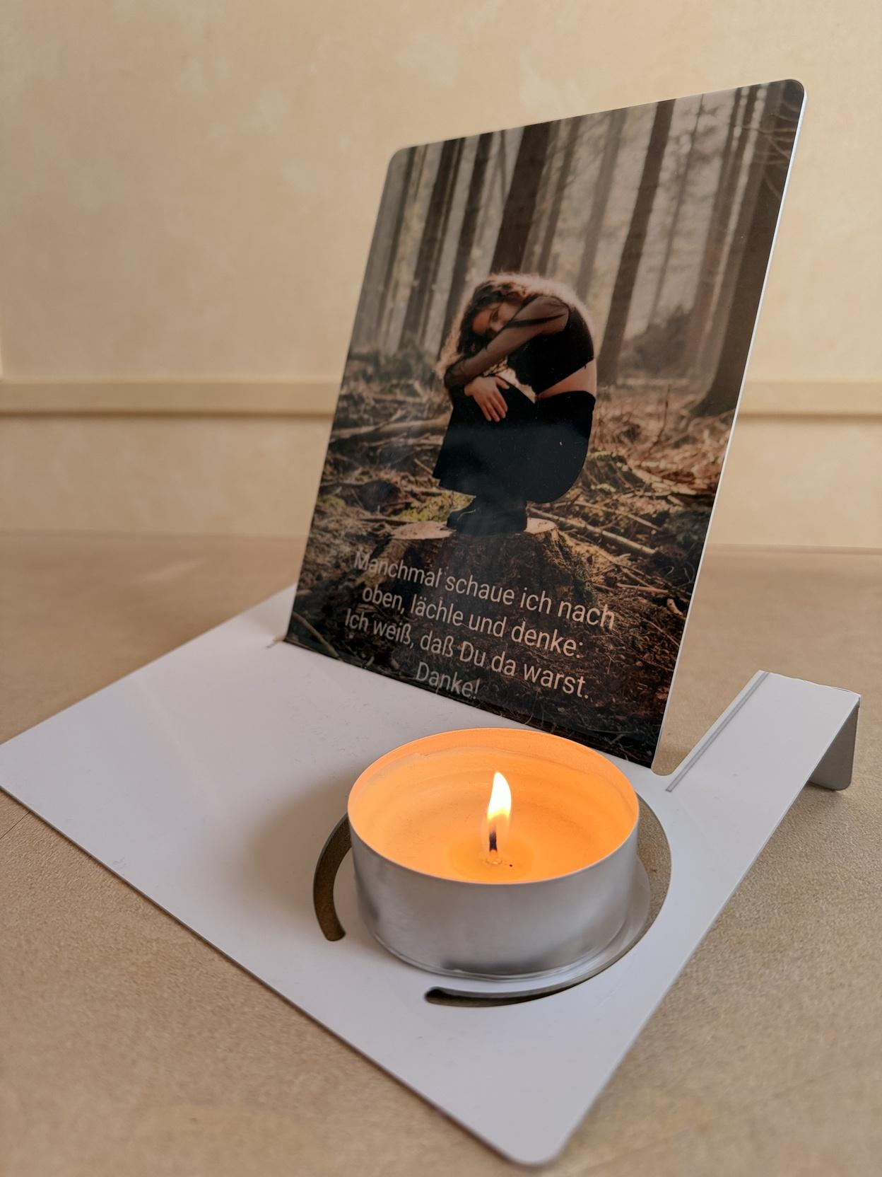 Karte mit einem Foto einer Frau im Wald und Text, daneben eine brennende Teelichtkerze auf einem wei&szlig;en Halter.
