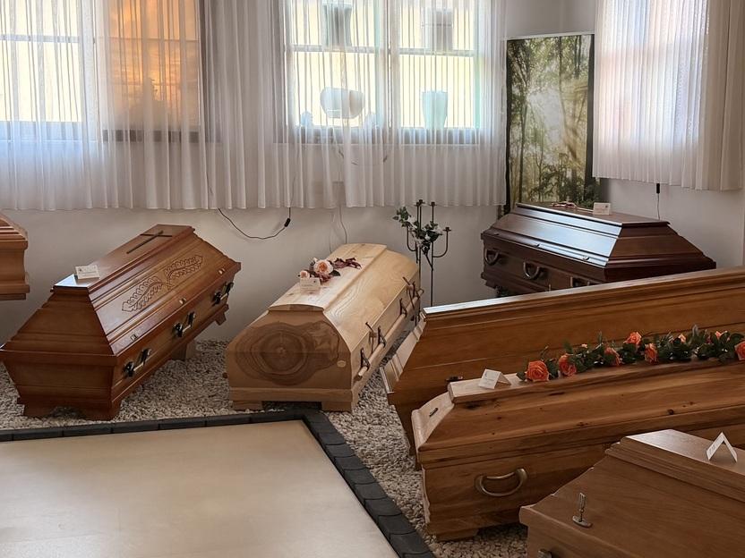 Ausstellung von mehreren S&auml;rgen in einem hellen Raume mit gro&szlig;en Fenstern und dekorativen Elementen.