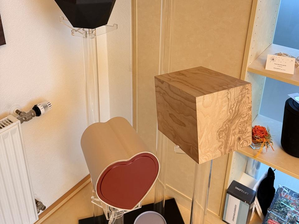 Vier verschiedene Designobjekte stehen auf transparenten St&auml;ndern: ein schwarzes, ein h&ouml;lzernes, ein rotes Herz und ein grauer Zylinder.