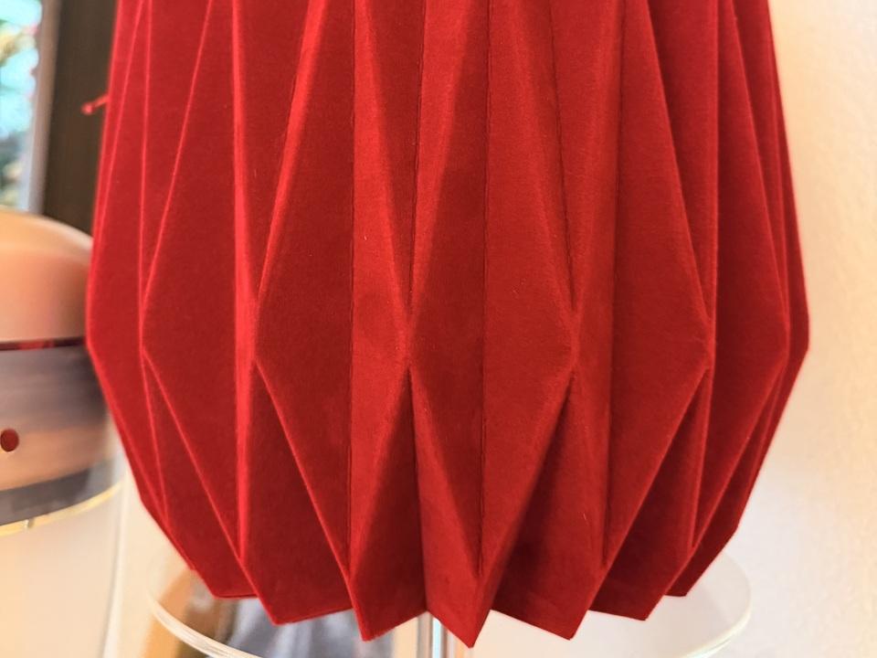 Rote, gefaltete Dekoration in Form einer Kugel steht auf einem Tisch.