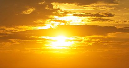 Sonnenuntergang mit goldenem Licht hinter bew&ouml;lktem Himmel, der den Horizont in warmen Farben erstrahlen l&auml;sst.
