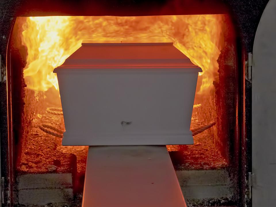 Einäscherungsanlage mit einem weißen Sarg, der in einen brennenden Ofen geschoben wird.