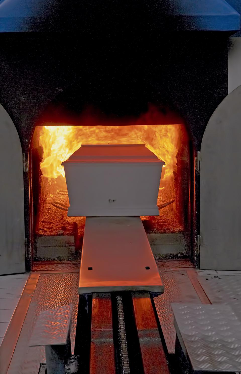 Einäscherungsanlage mit einem weißen Sarg, der in einen brennenden Ofen geschoben wird.