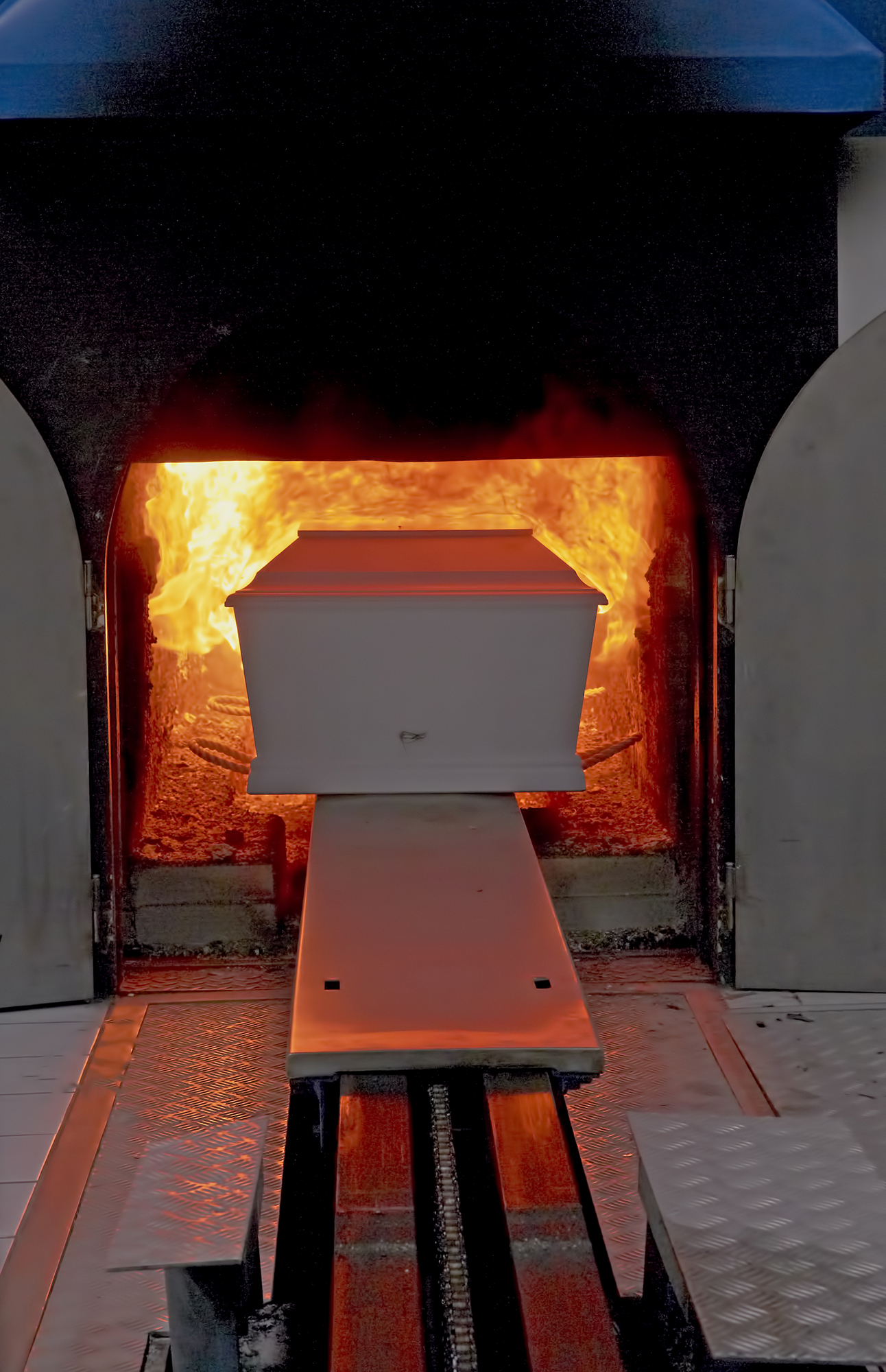 Einäscherungsanlage mit einem weißen Sarg, der in einen brennenden Ofen geschoben wird.