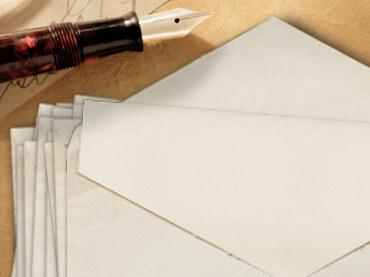 Stapel leerer Umschläge neben einer Feder und einem Schreibblock auf einem Holztisch.