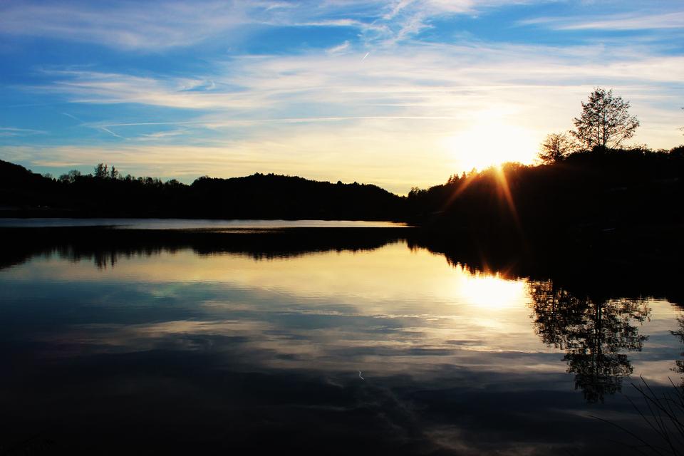 Sonnenuntergang über einem ruhigen See mit reflektierenden Bäumen und einem farbenfrohen Himmel.