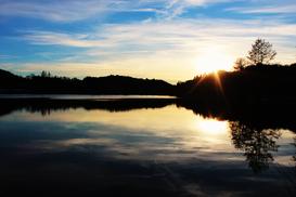 Sonnenuntergang über einem ruhigen See mit reflektierenden Bäumen und einem farbenfrohen Himmel.