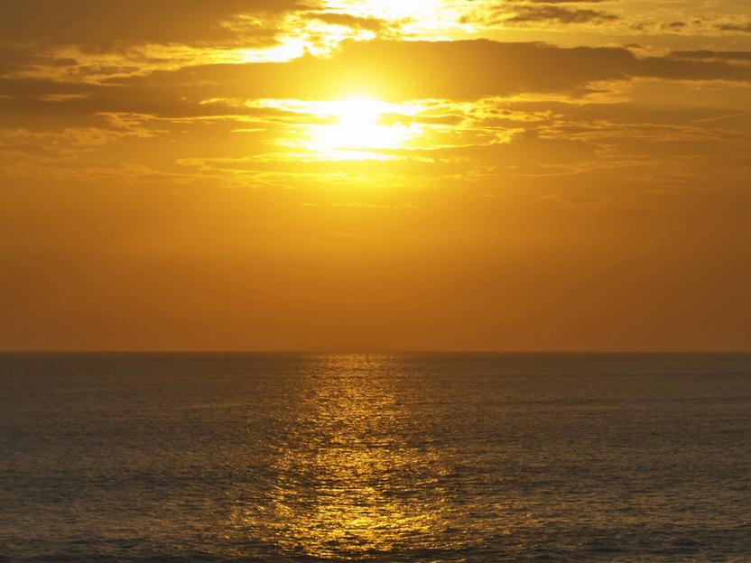 Sonnenuntergang über dem Meer, das sanftes goldenes Licht reflektiert, mit silhouettierten Felsen im Vordergrund.