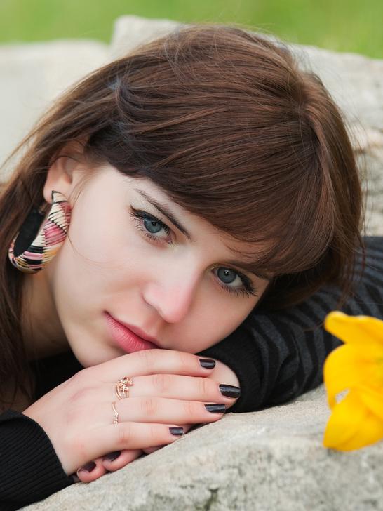 Junge Frau mit Blumen in der Nähe, die auf einem Stein liegt und in die Kamera schaut. Hintergrund mit grünem Gras.